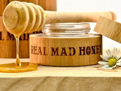 Verrückter Honig auf Holztisch Kleines Glas Wahnsinnshonig auf einem Holztisch mit einem Honigstab, der den Wahnsinnshonig auf den Tisch tropft
