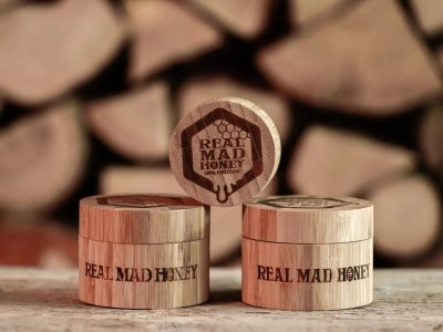 realmadhoney Logo aus Holz zwei echte, verrückte Honiggläser mit einem seitlichen Glas, das das Logo zeigt